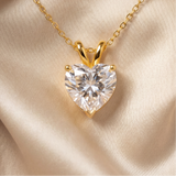 Heart-shaped diamond pendant on a gold chain against a beige satin background