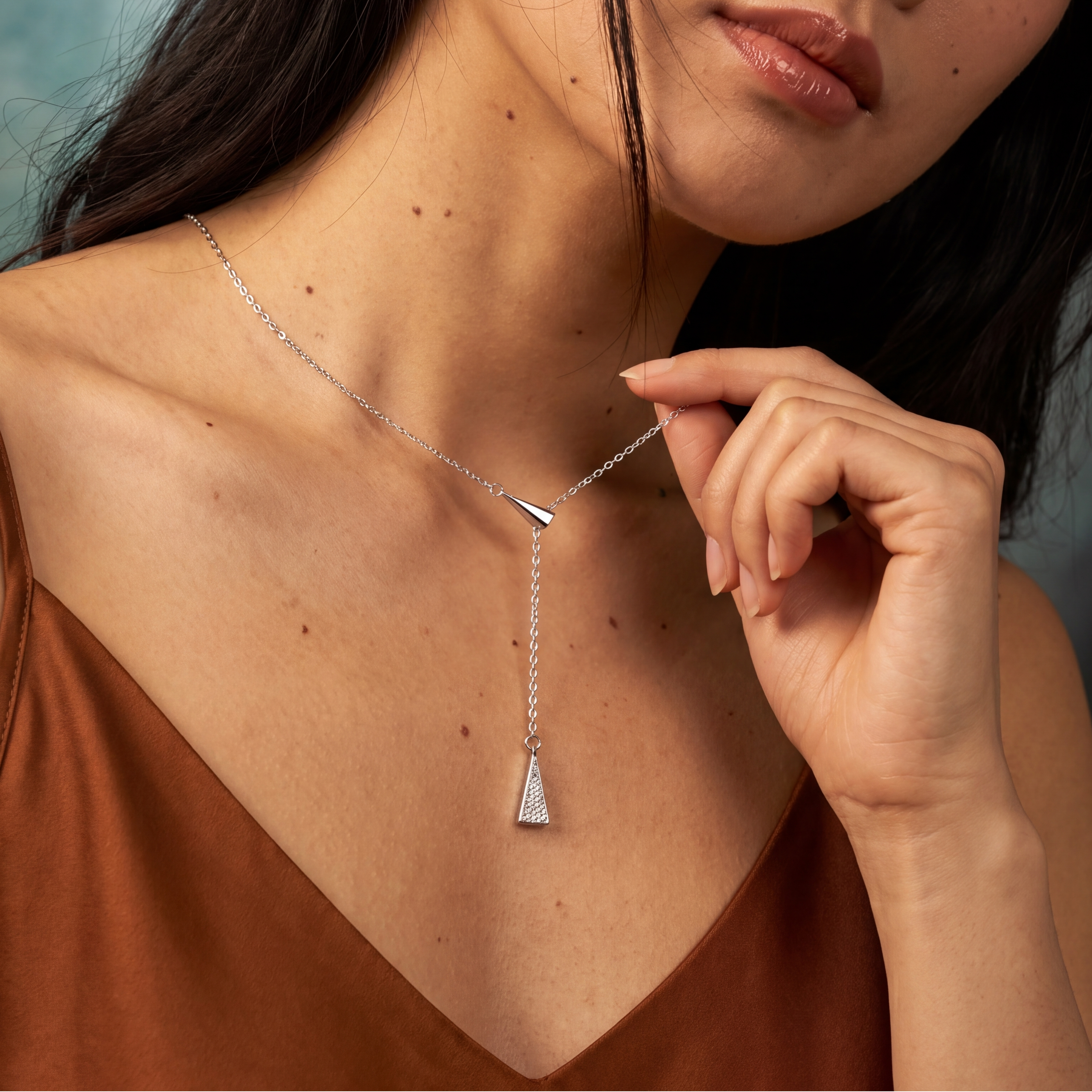 Woman wearing a silver necklace with a triangular pendant against a neutral background
