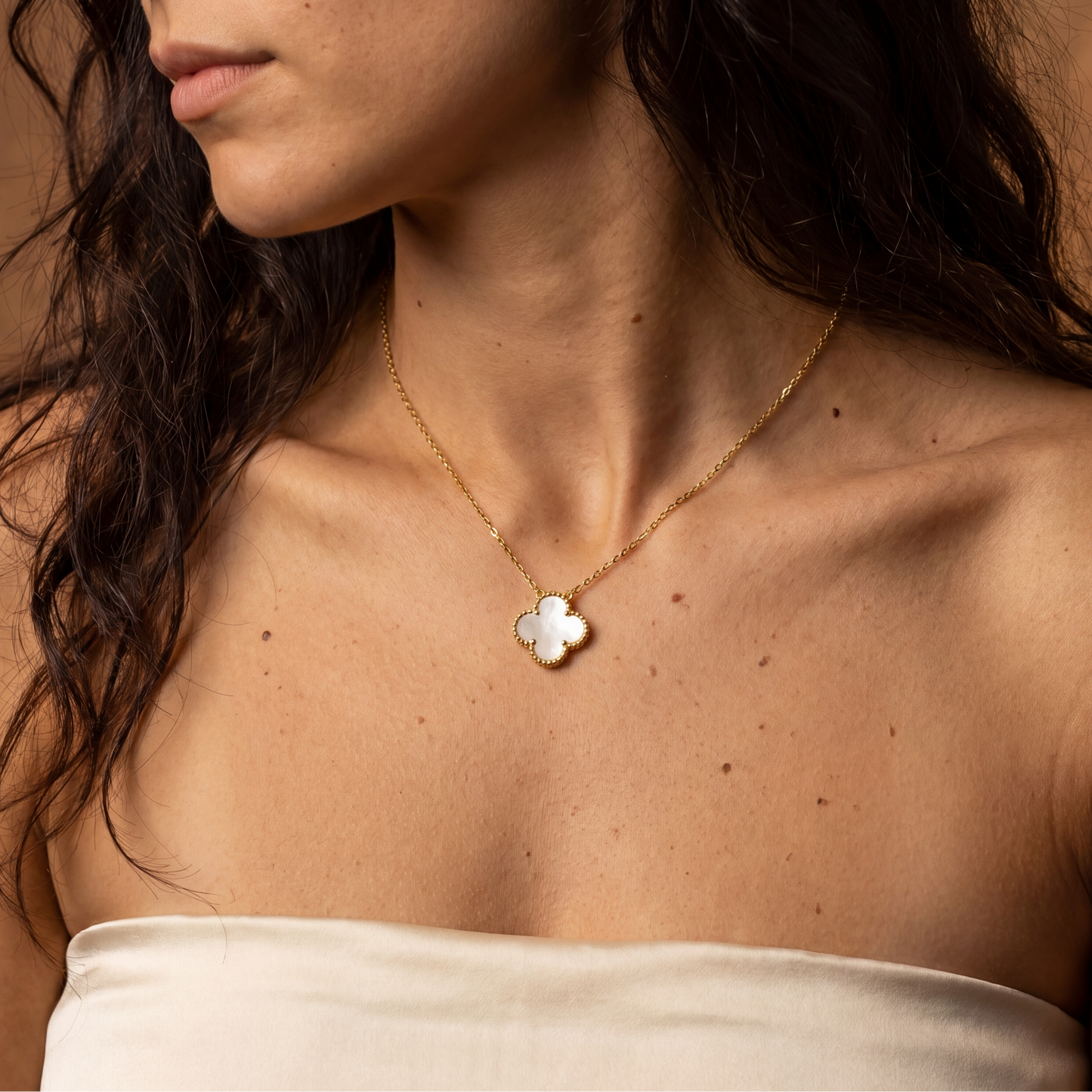 Close-up of a woman wearing a gold necklace with a clover pendant against a warm brown background.