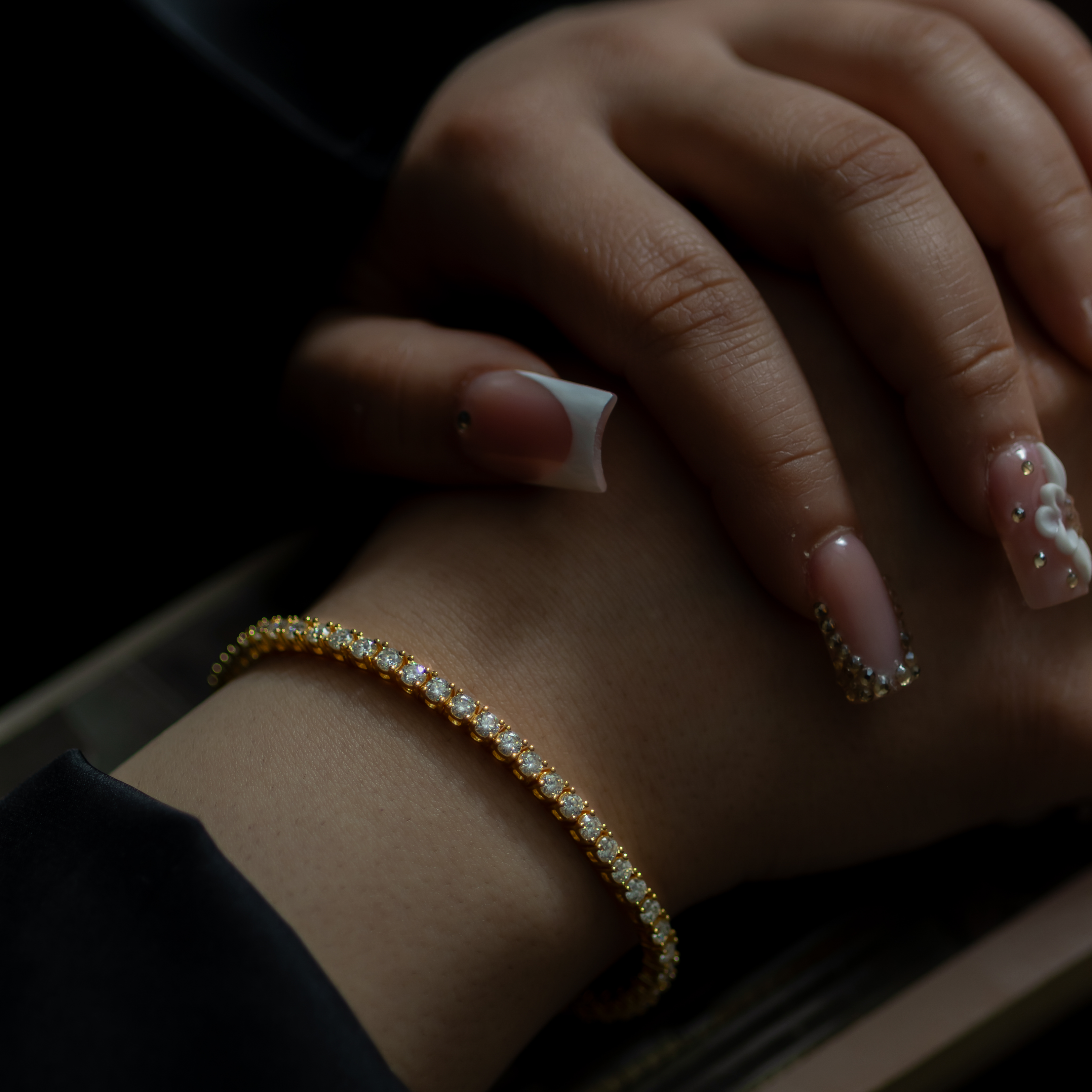 Close-up of a hand with a bracelet and nail art on a dark background
