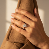 Hand wearing a diamond ring holding a brown coat with a neutral background