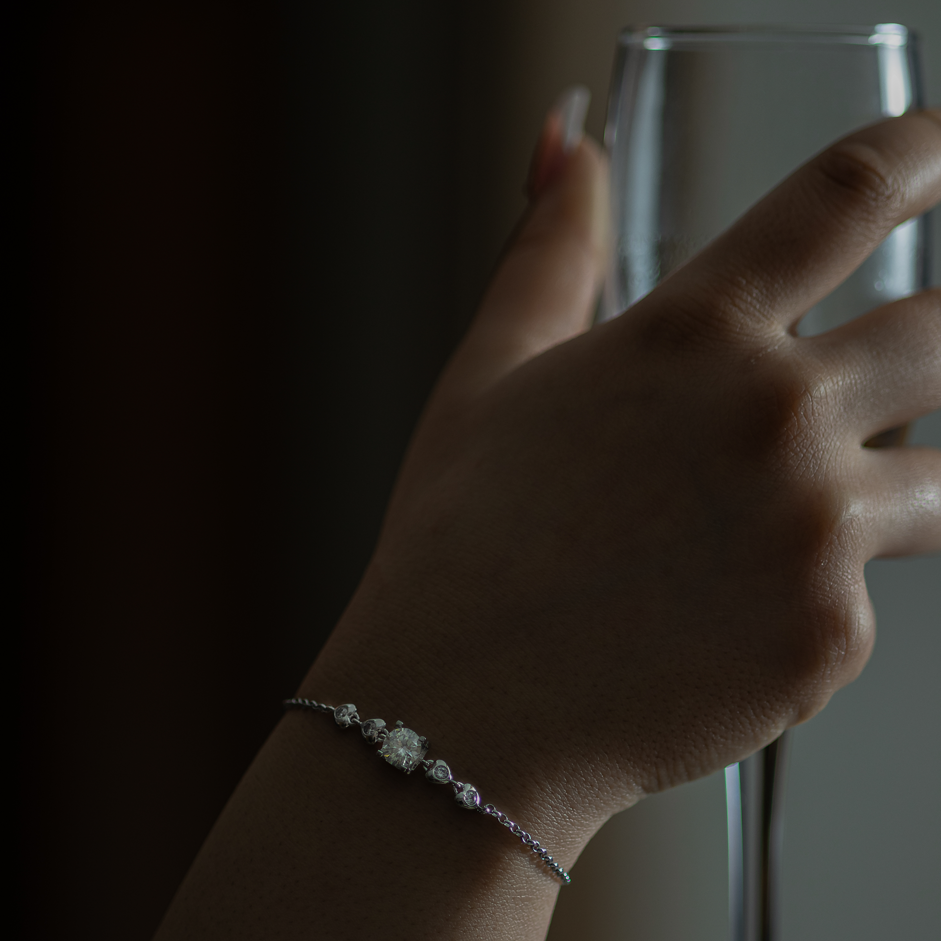 Hand wearing a bracelet with a glass in the background