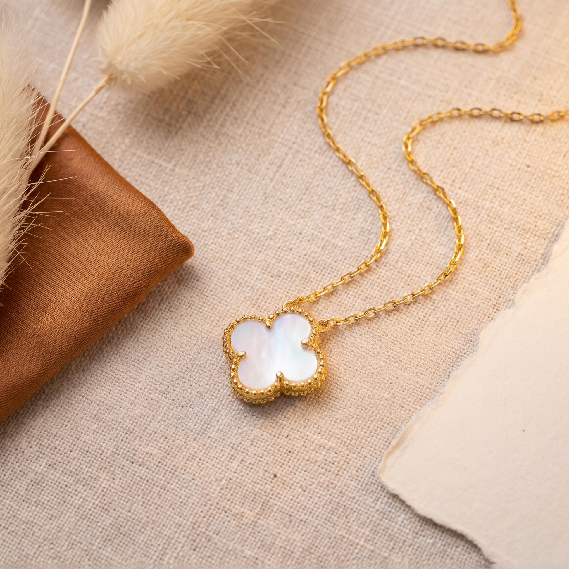Gold necklace with a white pendant on a textured beige surface