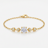 A delicate yellow gold chain bracelet featuring a central square-cut clear gemstone, flanked by three small heart-shaped clear gemstones in gold settings, photographed on a clean white background.