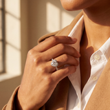 Person wearing a brown coat and white shirt with a diamond ring on a neutral background