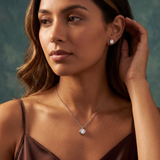 Woman wearing diamond earrings and necklace against a neutral background