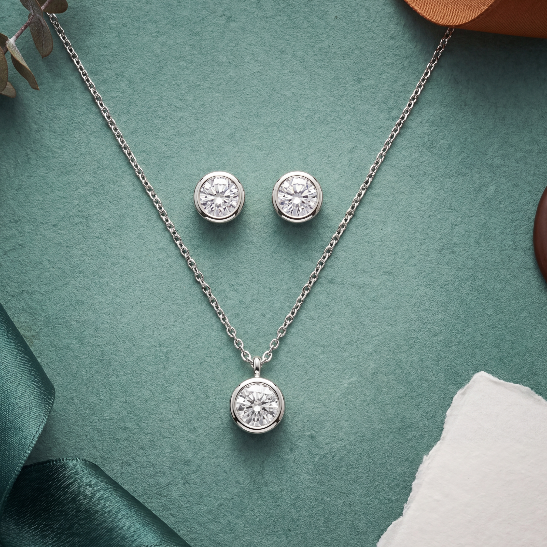 Silver jewelry set with necklace and earrings on a textured surface with ribbons and leaves.
