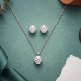 Silver jewelry set with necklace and earrings on a textured surface with ribbons and leaves.