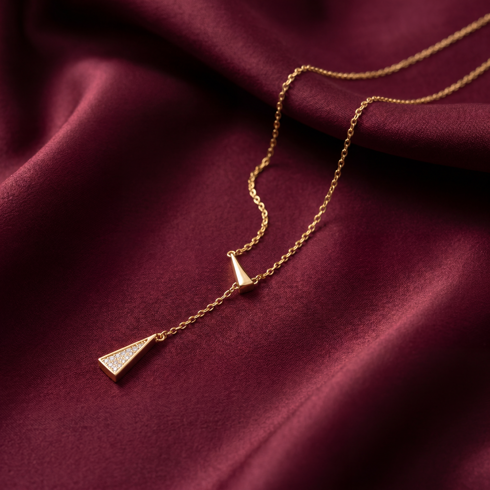 Gold necklace with a triangular pendant on a burgundy fabric background