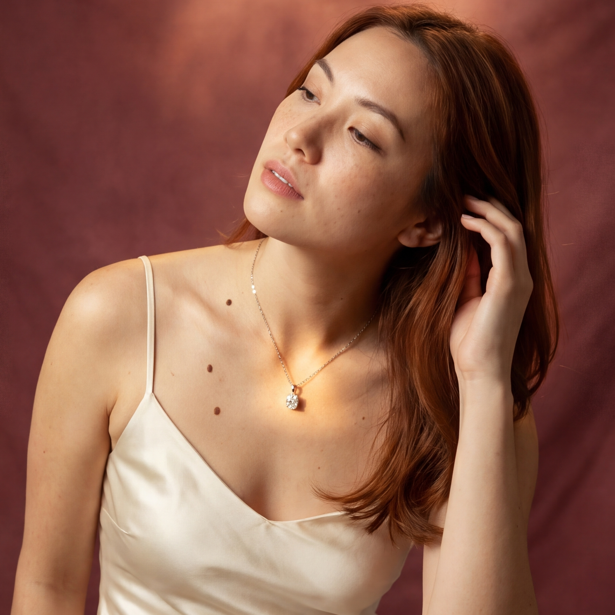 Woman in a white dress sitting on a wooden stool against a maroon backdrop