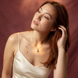 Woman in a white dress sitting on a wooden stool against a maroon backdrop