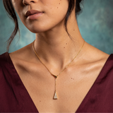 Woman wearing a gold necklace with a triangle pendant against a textured blue background