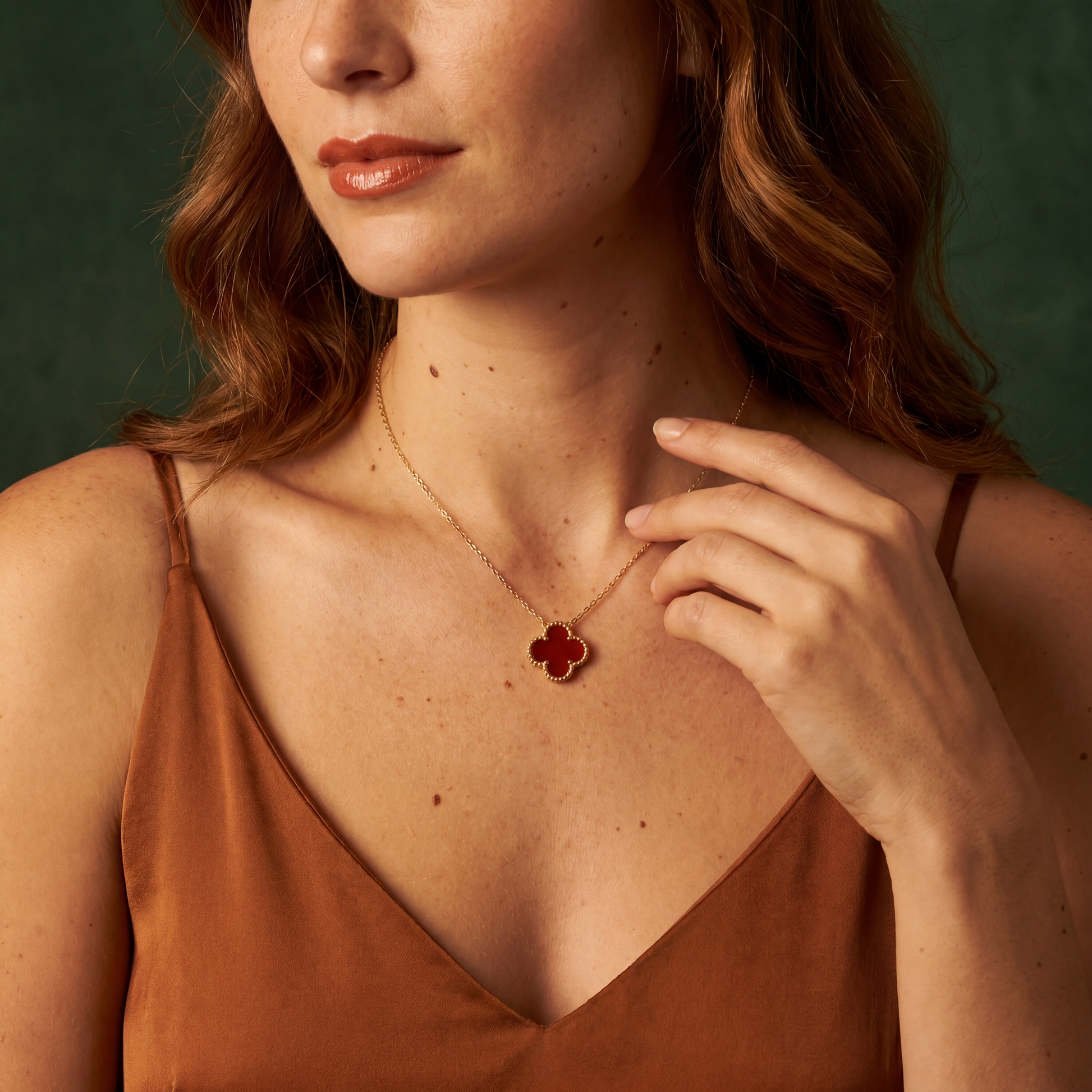 Woman wearing a gold necklace with a red pendant against a green background