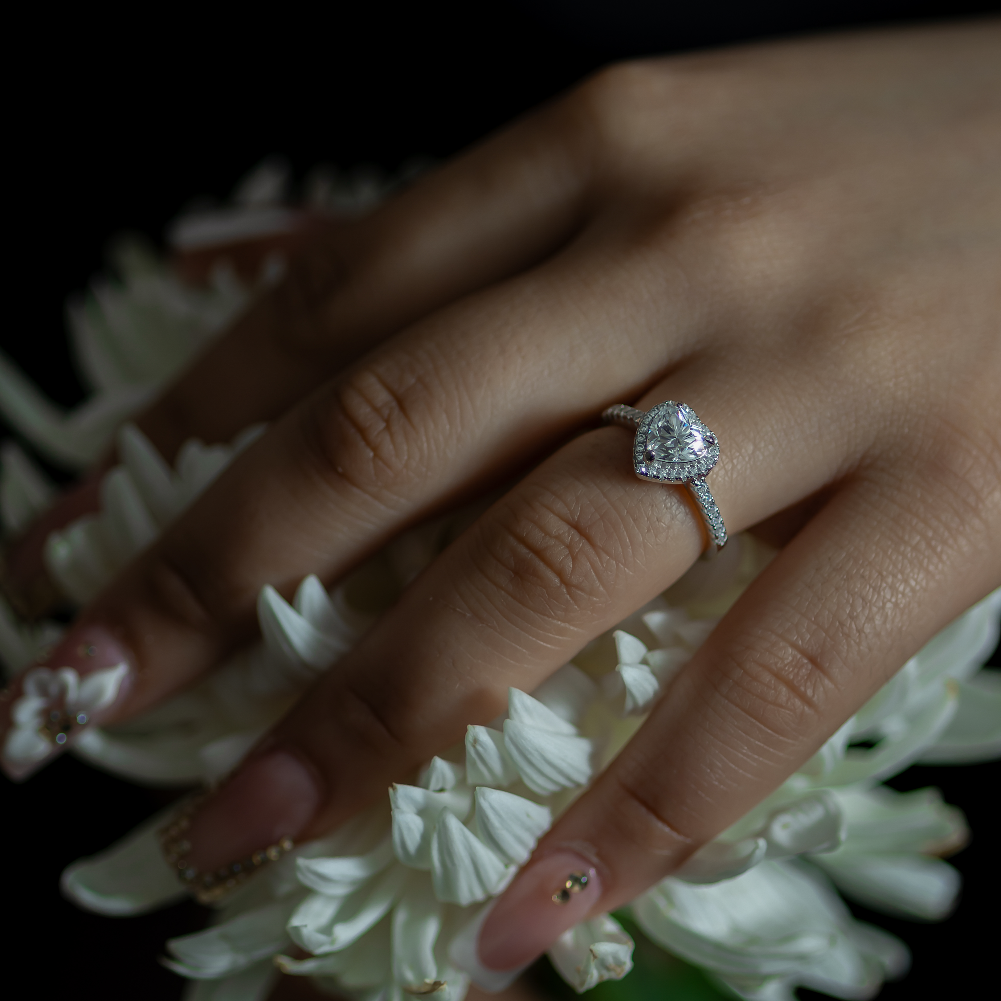 Hand wearing a diamond ring with white flowers in the background