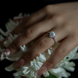 Hand wearing a diamond ring with white flowers in the background