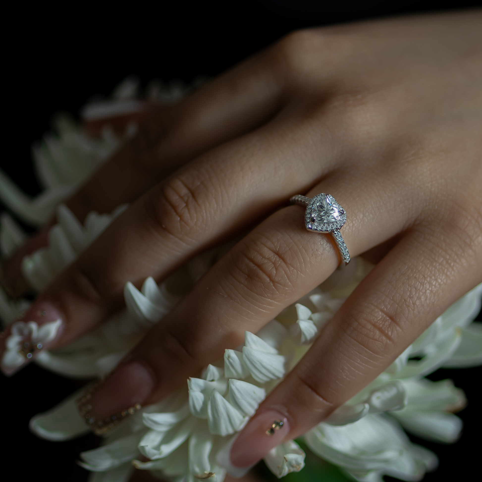 Hand wearing a diamond ring with white flowers in the background