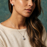 Woman wearing a necklace with a pendant against a textured green wall.