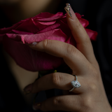 Close-up of a hand holding a pink rose with two rings on fingers against a dark background